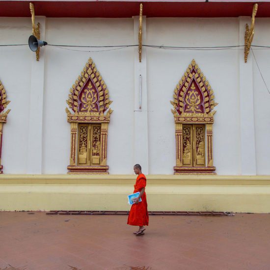 Jeune moine avec son cahier d'écolier passant devant un templs à Vientiane, Laos