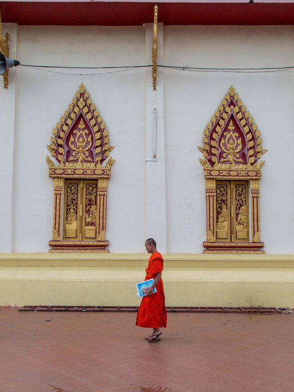 Jeune moine avec son cahier d'écolier passant devant un templs à Vientiane, Laos